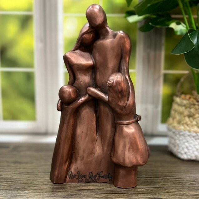 A copper family of four sculpture with two children hugging their parents in a Family Hug! The front of the sculpture is engraved with "Our Love, Our Family"