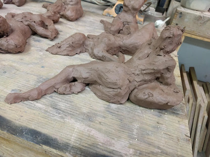 This sculpture is a study of the human form, capturing a reclining figure with an emphasized gesture. It is a beginner's piece in figure sculpture, sculpted in water-based clay, and measures approximately 9 inches in length. The work, showing a figure in a pose that suggests contemplation or rest, was created by Elizabeth Bonura.