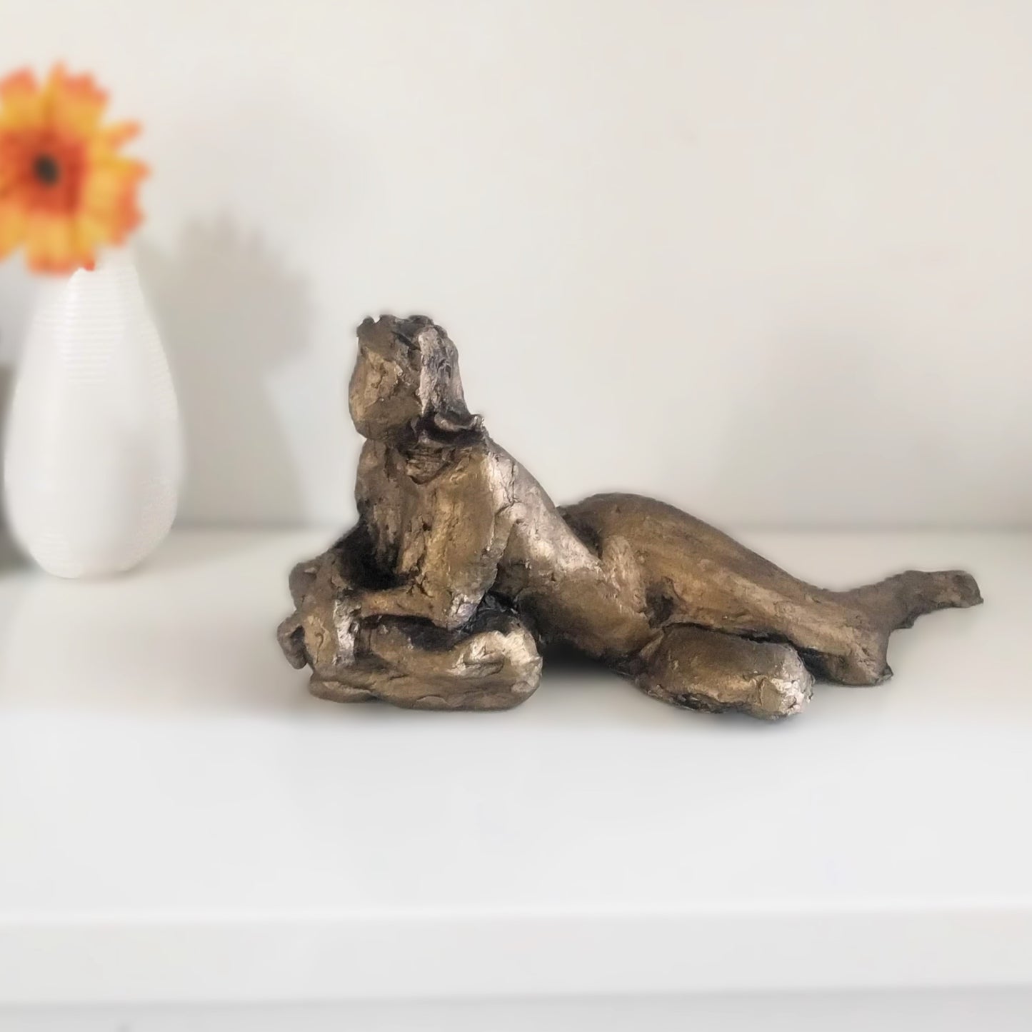 This sculpture is a study of the human form, capturing a reclining figure with an emphasized gesture. It is a beginner's piece in figure sculpture, sculpted in water-based clay, and measures approximately 9 inches in length. The work, showing a figure in a pose that suggests contemplation or rest, was created by Elizabeth Bonura.